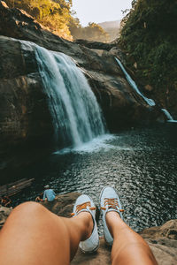 Low section of woman on rock against waterfall