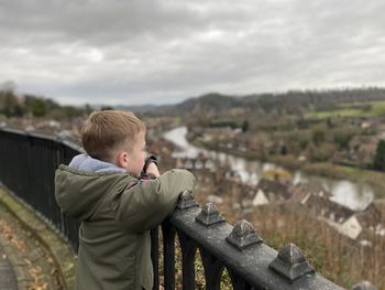 Boy standing by railing against sky