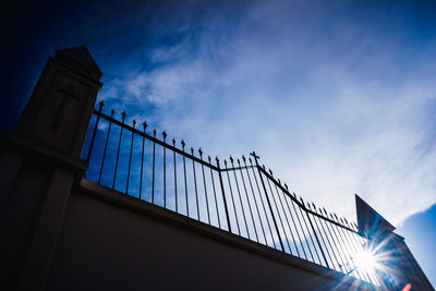 Low angle view of illuminated fence against blue sky