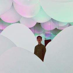 Portrait of young woman with balloons standing against ceiling