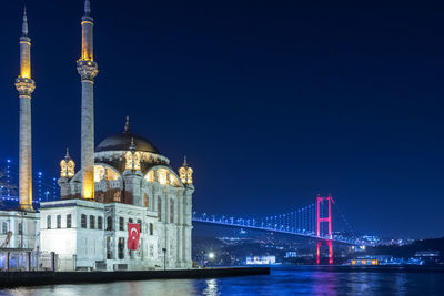 Illuminated bridge over river against sky in city at night