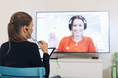 Rear view of businesswoman using in-ear headphones while video conferencing in creative office