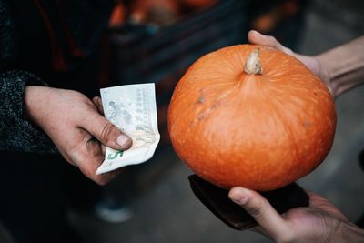 Cropped image of people exchanging pumpkin with paper currency outdoors