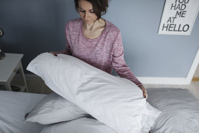 High angle view of woman arranging pillows on bed at home