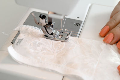 A woman, sews lace white underwear behind a sewing machine.