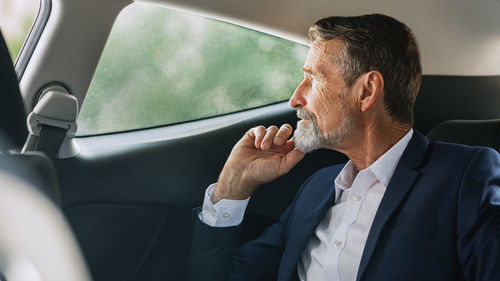 Thoughtful senior businessman looking through car window