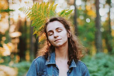 Eyes closed young woman with leaves on behind in forest