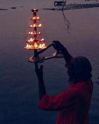 Man holding oil lamp while standing by lake