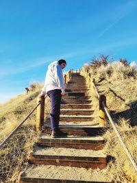 Rear view of man walking on steps against clear blue sky