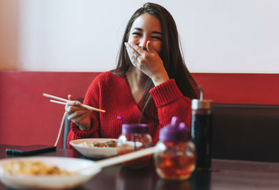Beautiful smiling young asian woman in red clothes eating asian food with chopsticks in chinese cafe