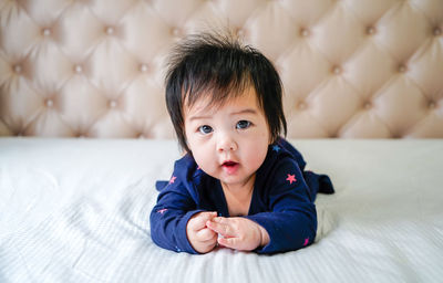 Portrait of cute baby girl lying down on bed at home