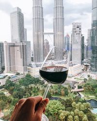 Cropped image of person holding wineglass against buildings in city