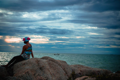 Man sitting on rock looking at sea shore against sky