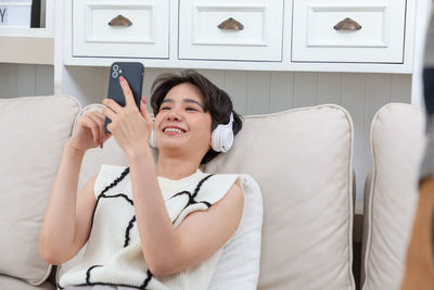 Young woman using mobile phone while sitting on bed at home