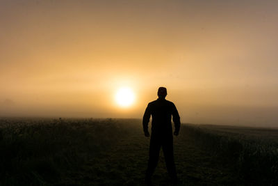 Silhouette man standing on field against sky during sunset