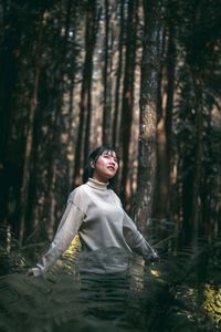 Woman standing by tree trunk in forest