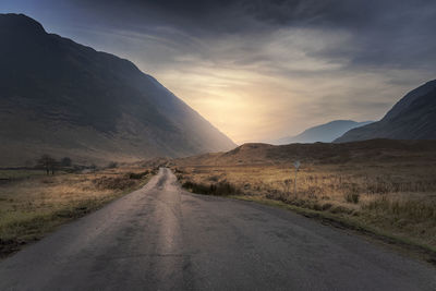 Dirt road leading towards mountains against sky