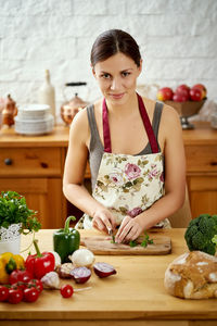 Portrait of smiling young woman preparing food at kitchen