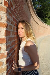 Side view portrait of woman standing by brick wall