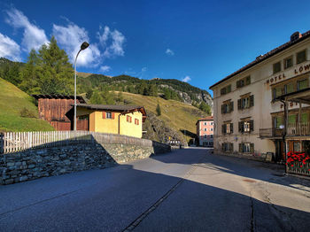 Road by buildings against blue sky