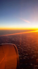 Cropped image of airplane flying over sea during sunset