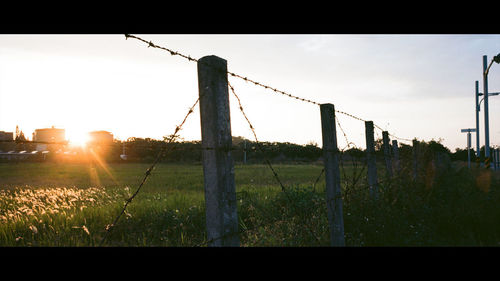 Fence on field against sky during sunset