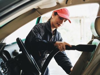 Young woman cleaning car with vacuum cleaner in workshop