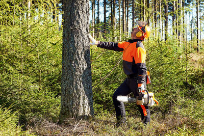 Professional lumberjack with protective workwear and chainsaw working in a forest