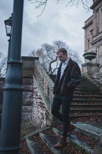 Full length of young man looking away while moving down on staircase against sky