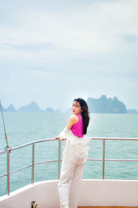 Side view of woman sitting on railing against sea