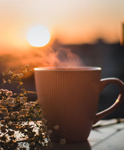 Close-up of coffee mug against sky during sunset