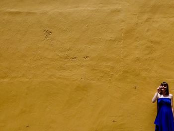 Beautiful woman in blue dress standing against yellow wall