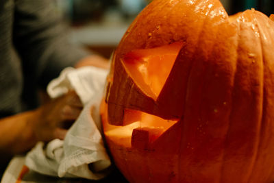 Cropped hands of person carving pumpkin on table at home