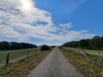 Road amidst field against sky