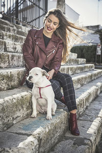 Full length of smiling young woman with dog sitting on steps