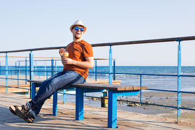 Man sitting on railing by sea against clear sky