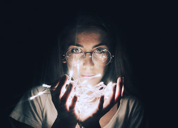 Portrait of young woman holding illuminated string lights in darkroom