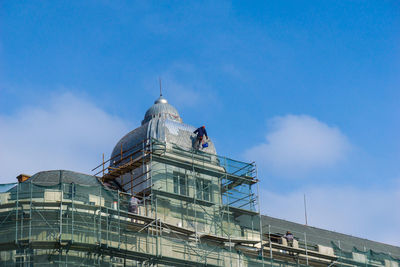 Men painting built structure against sky