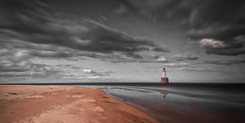 Lighthouse on beach against sky during sunset