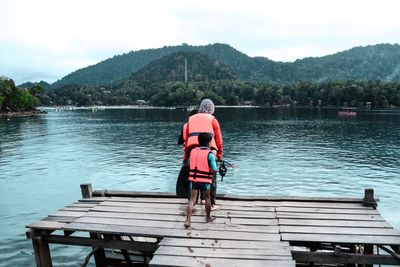 Rear view of family with life jackets and snorkel while standing on pier over lake