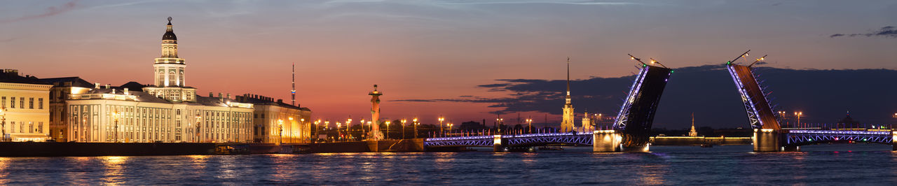 View of illuminated buildings by river against sky