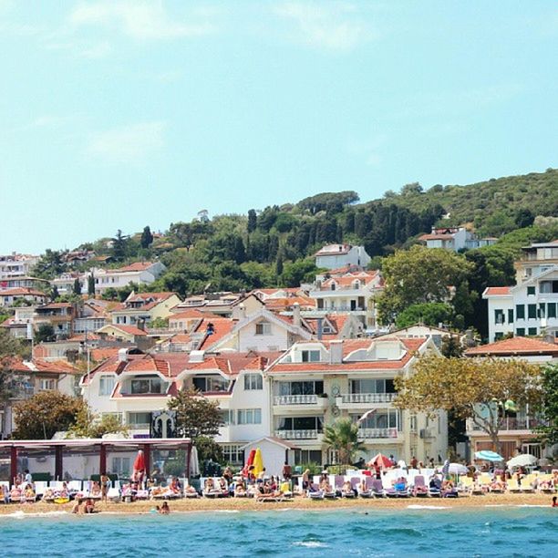 building exterior, architecture, built structure, water, waterfront, tree, house, residential structure, sea, residential building, sky, town, large group of people, blue, day, river, residential district, townscape, mountain