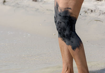 Midsection of woman with black mud on knees standing at beach