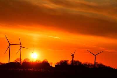 Silhouette wind turbines on field against orange sky