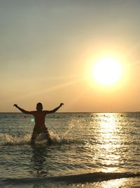 Silhouette man in sea against sky during sunset