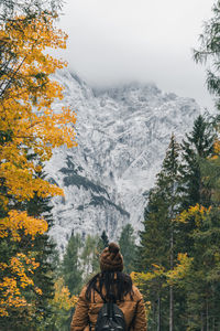 Rear view of woman wearing warm clothes and knit hat, walking toward mountains in autumn