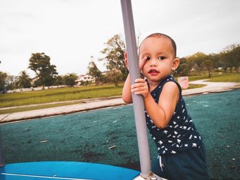 Portrait of cute boy holding pole while standing on seat at park