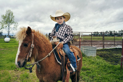 Portrait of cute cowboy riding horse on ranch