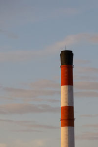 Lighthouse by factory against sky