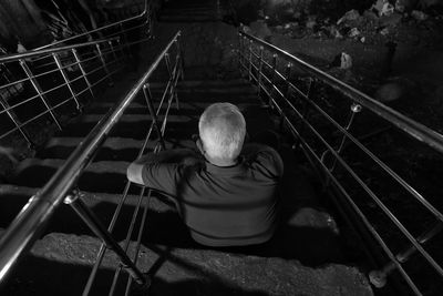 Rear view of man sitting on railing